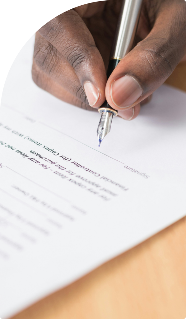 A close-up of a person signing a business contract with a silver fountain pen on a wooden desk, symbolizing legal agreements and professional commitments.