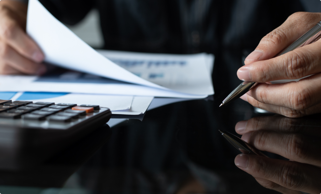 A close-up of a professional reviewing financial documents with a pen in hand, alongside a calculator, symbolizing accounting, financial planning, and decision-making.