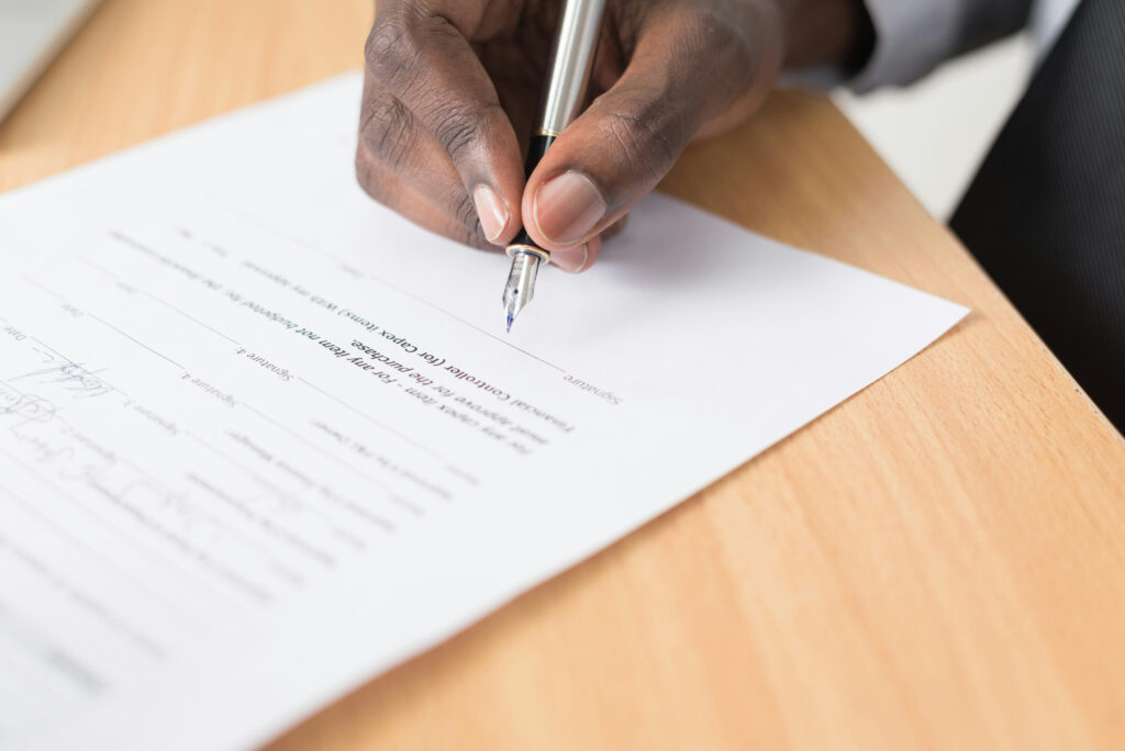 Close-up of businessman signing legal documents on a desk, representing essential paperwork for UAE free zone business formation.