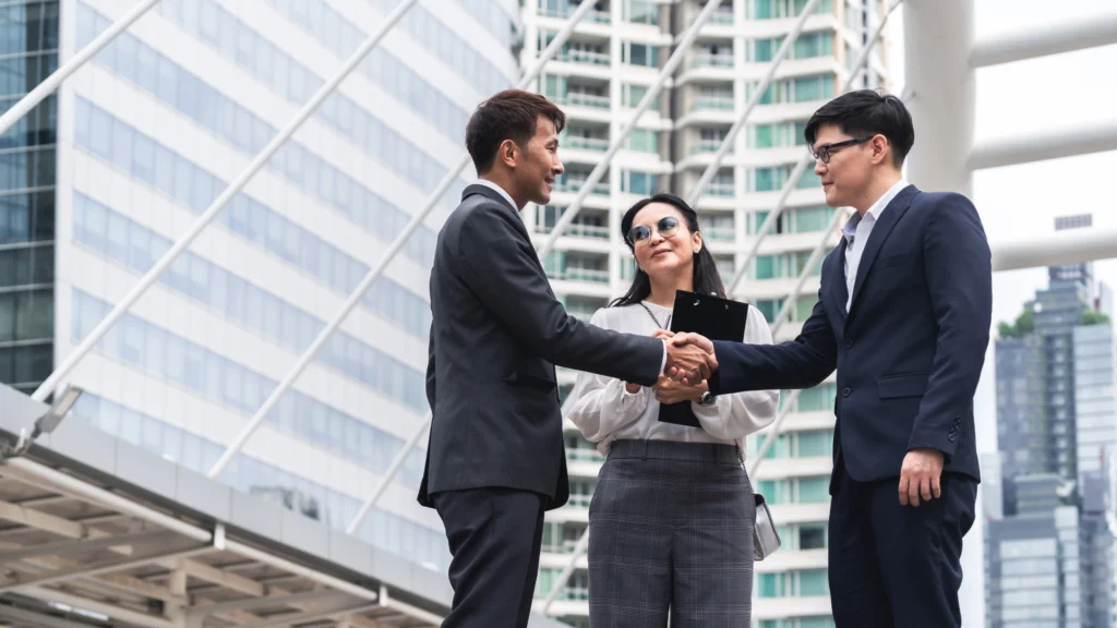 two people shaking hands after a business meeting while another person smiles
