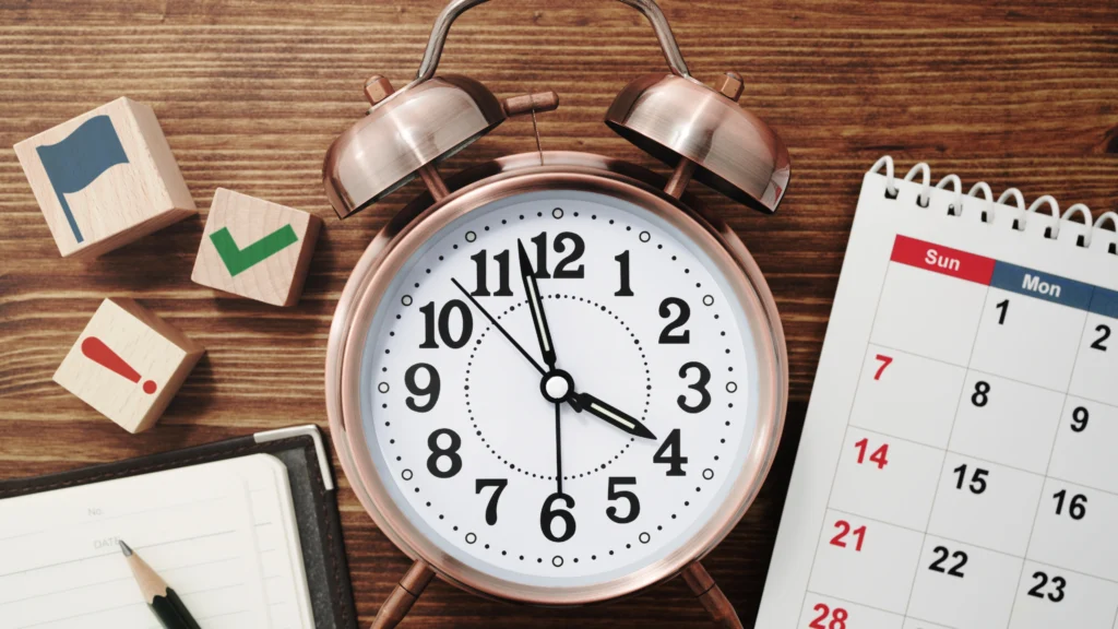 an alarm clock on a work desk next to a calendar