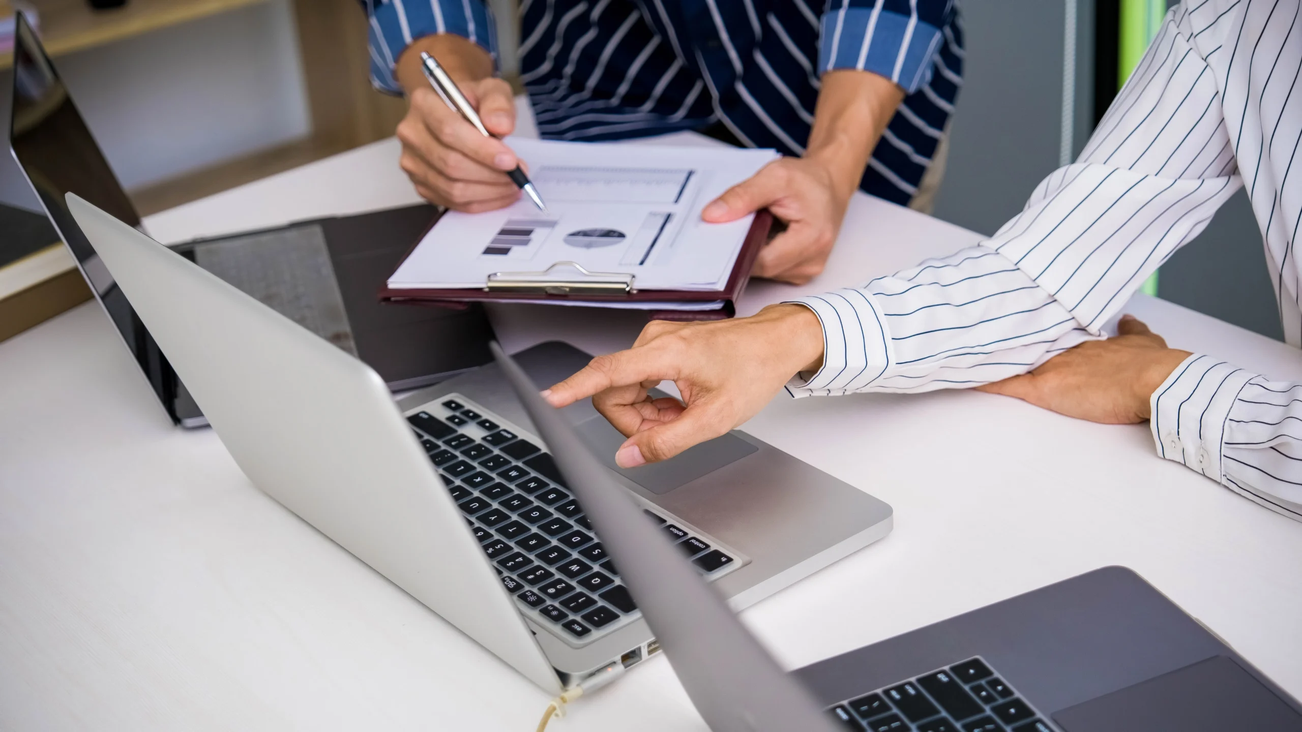 two people looking at a laptop while one goes over an important page