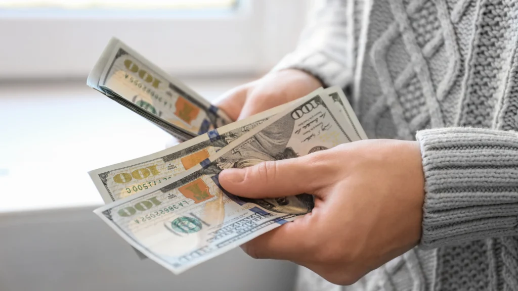 a person counting several 100 dollar bills in their hands