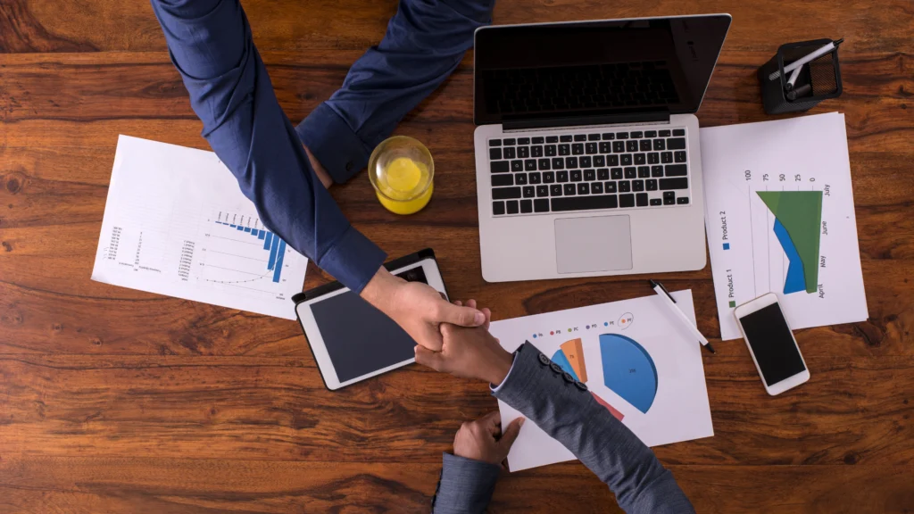 two men shaking hands from across their work table