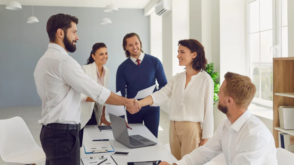 two people shaking hands while others around them smile