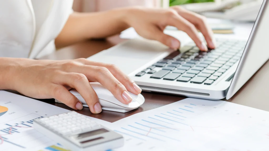 a person using their laptop with important documents and things beside them