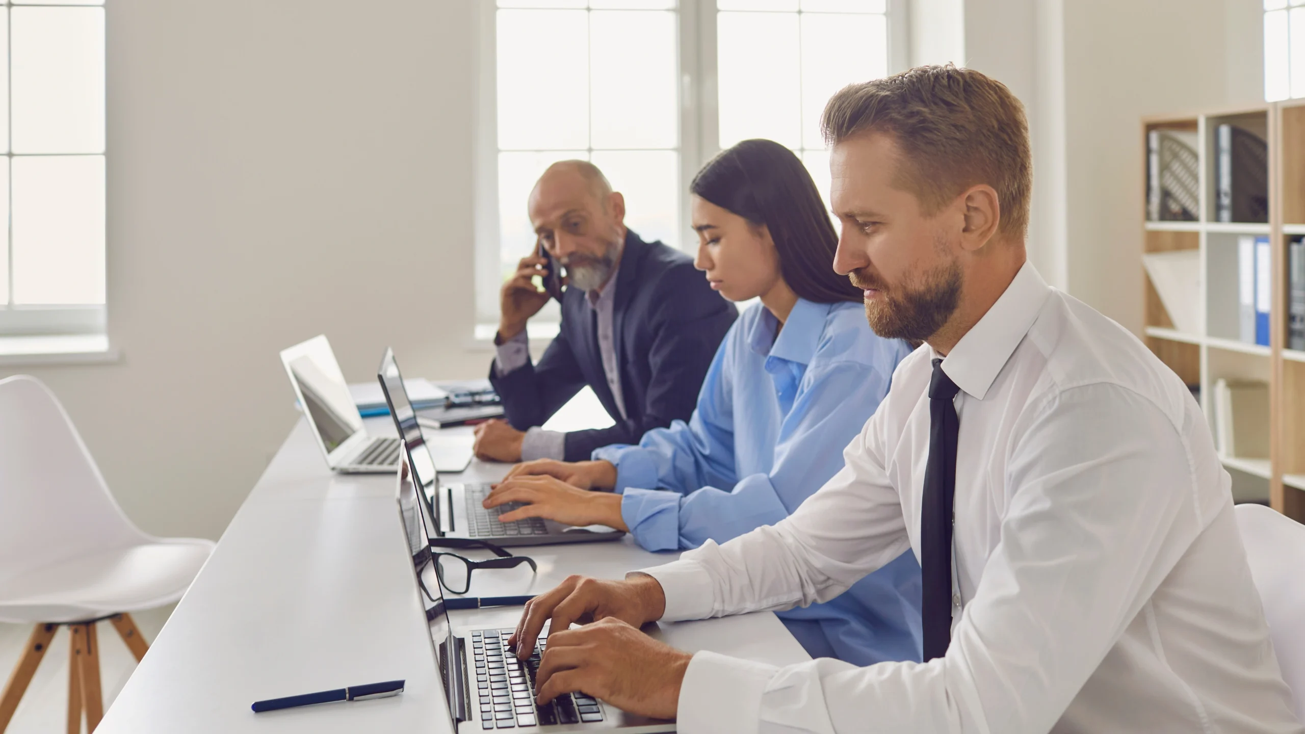 a man on his phone in the office while two other employees are working