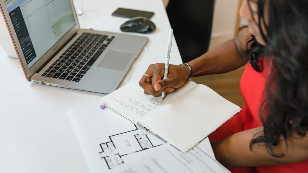 a woman noting things down on a document while working on her laptop