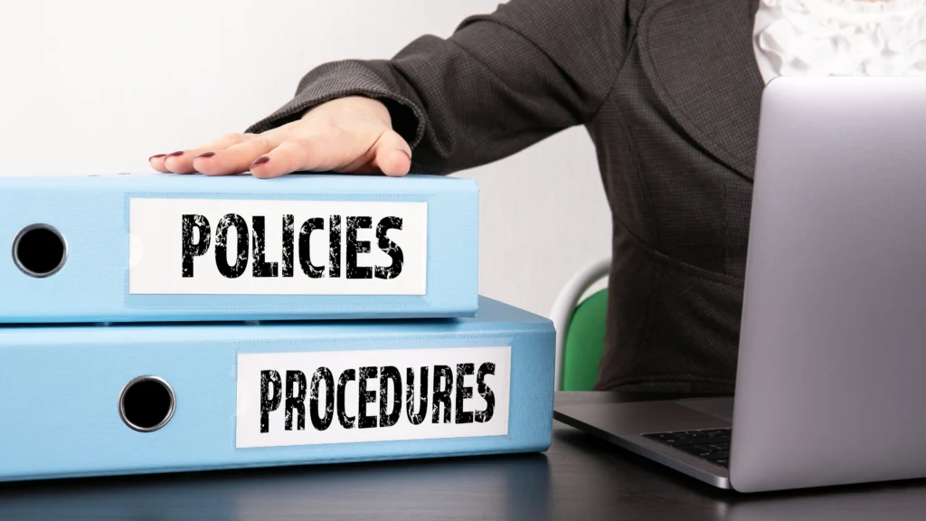 a man with his hand on two foldeers that say policies and procedures