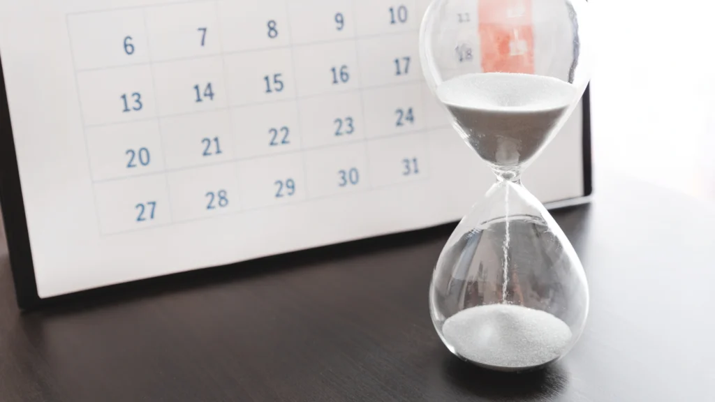 An hourglass in front of a calendar to symbolise time passing