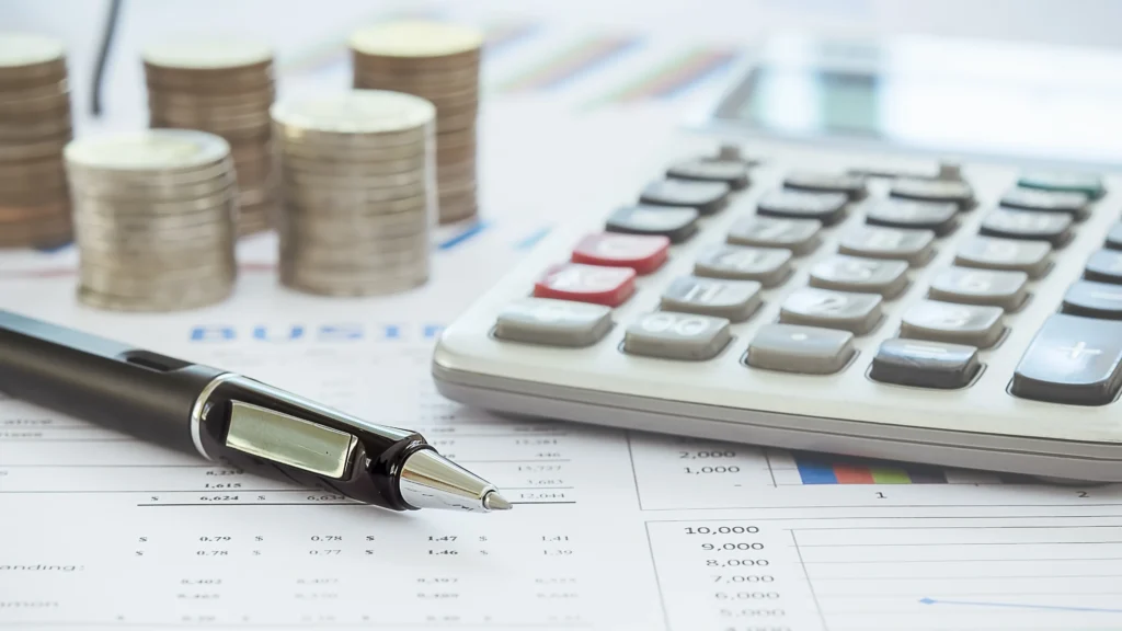 a pen, calculator, and stacks of coins on a table on top of important documents