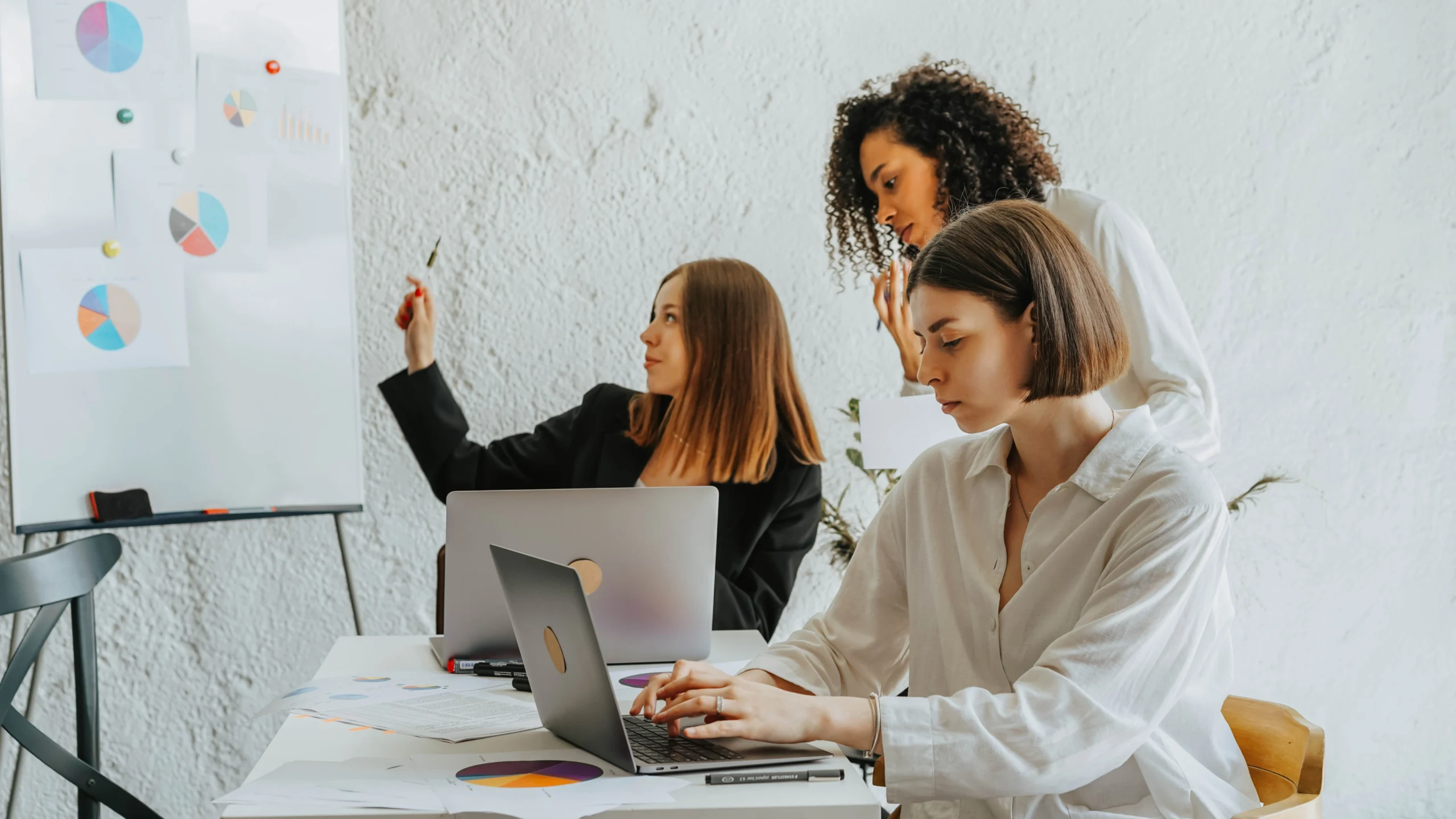 A woman working on her laptop while two colleagues are nearby