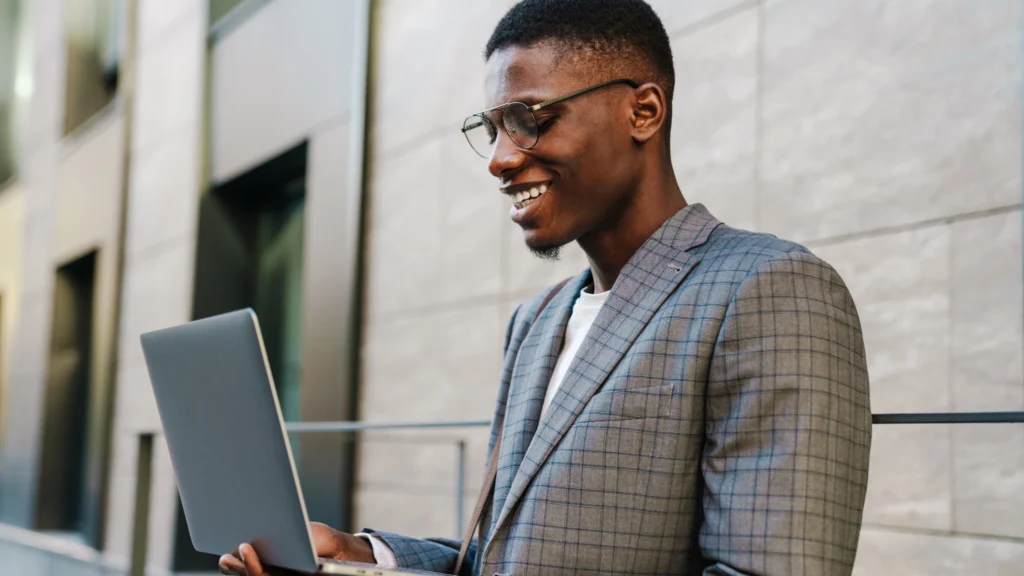 a man smiling and using his laptop outside of his workplace
