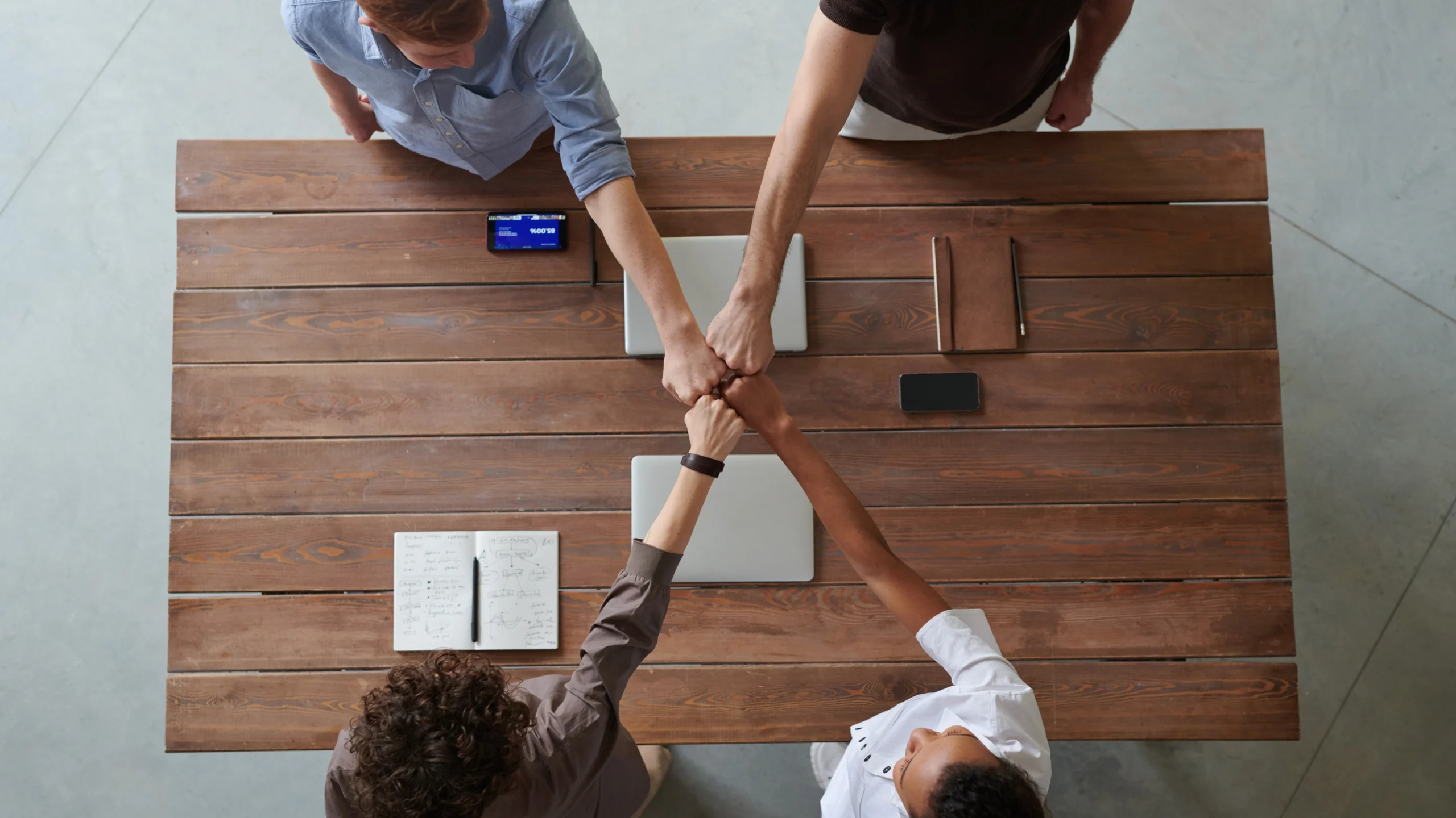 four people around a table holding their fists together