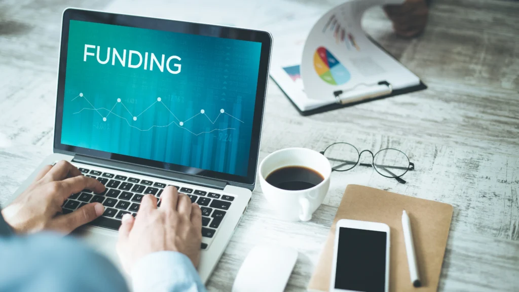 Person working on a laptop with the word funding in focus