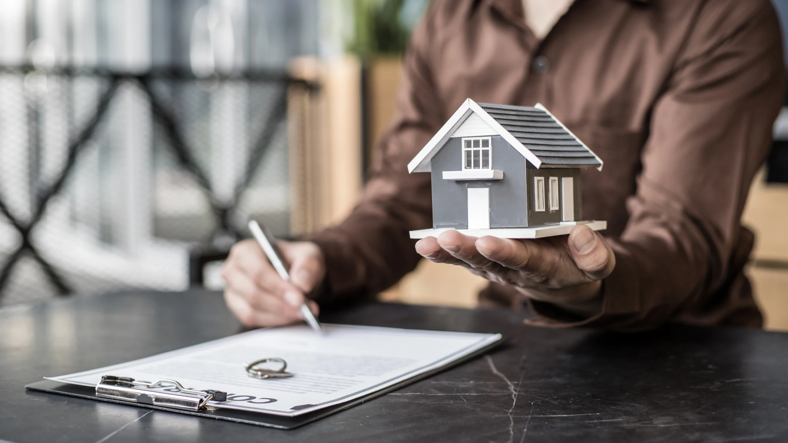 man signing papers while holding up a small toy house to represent real estate