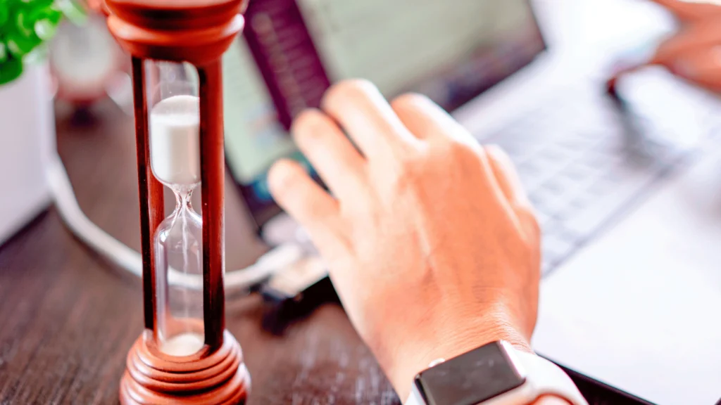 an hourglass next to a person working on their laptop