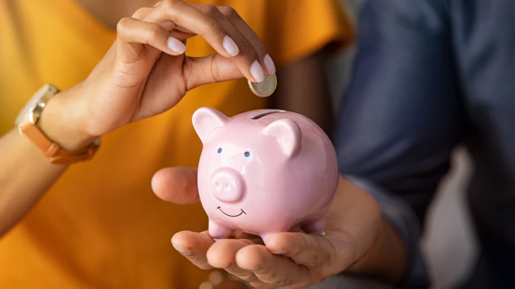 two people putting money into a piggy bank to symbolise their savings